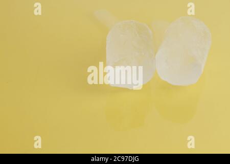Closeup shot of two pieces of ice on a yellow surface Stock Photo