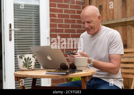 Man using laptop and mobile phone in garden Stock Photo