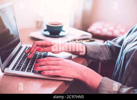 Anonymous female freelancer typing on laptop while working remotely from home at wooden table with books Stock Photo