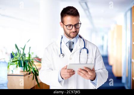 Shot of male doctor using digital tablet while standing on the hospital foyer and working. Stock Photo