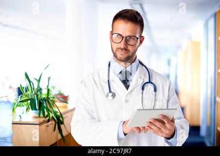 Shot of thinking male doctor using digital table and working while standing on the hospital foyer. Stock Photo