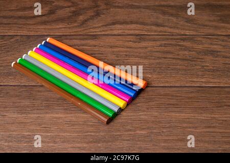 A lot of multi-colored colorful vibrant felt-tip pens on a brown wooden background. Stock Photo