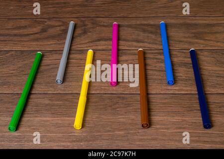 A lot of multi-colored colorful vibrant felt-tip pens on a brown wooden background. Stock Photo