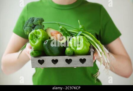High angle of anonymous female in green t shirt showing container with ripe healthy vegetables