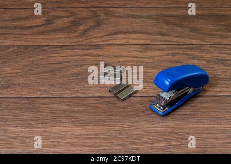 Blue stapler and staples on a brown wooden background. For business and office. Stock Photo