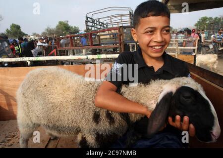 Khan Younis, Gaza. 29th July, 2020. Gaza, Palestine. 29th July 2020. Palestinian boy smiles as Muslims buy sacrificial animals at a livestock market ahead of the Eid al-Adha (feast of sacrifice) in Khan Yunis in the southern Gaza Strip, Wednesday, July 29, 2020. Muslims around the world celebrate Eid al-Adha to mark the end of the Haj by slaughtering sheep, goats, cows and camels to commemorate Prophet Abraham's willingness to sacrifice his son Ismail on God's command. Photo by Ismael Mohamad/UPI Credit: UPI/Alamy Live News Stock Photo