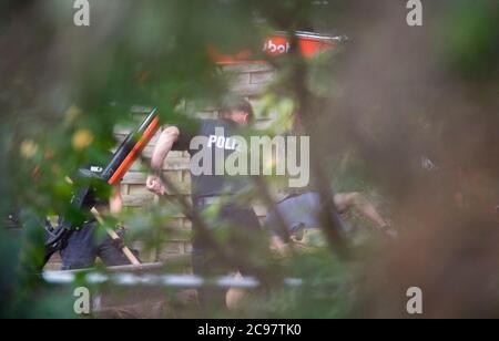 Seelze, Germany. 29th July, 2020. Police officers stand with shovels next to an excavator in an allotment garden in the Hanover region. In the case of the missing little Maddie McCann, police are continuing the excavation work in an allotment garden near Hanover. Credit: Julian Stratenschulte/dpa/Alamy Live News Stock Photo