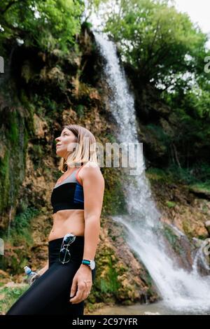 Young female nature explorer standing by the waterfall Stock Photo