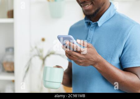 African young man typing a message on his mobile phone while drinking coffee in the morning Stock Photo