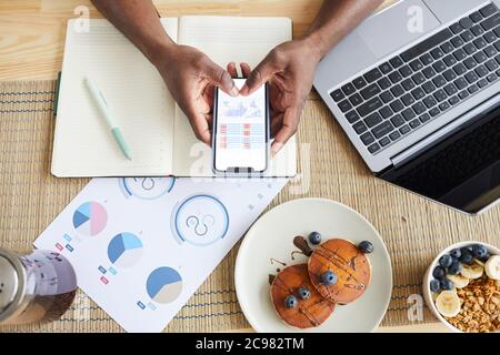 High angle view of man examining the business charts on his mobile phone while working at the table during breakfast Stock Photo