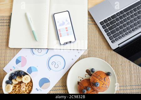 High angle view of business documents with charts and graphics with laptop and breakfast on the table at home Stock Photo
