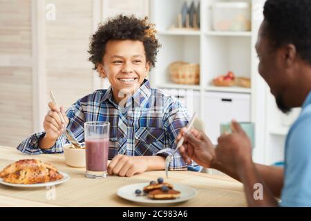 African boy with curly hair smiling to his father while they having breakfast together in the kitchen Stock Photo