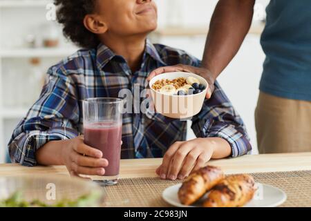 Close-up of African boy eating cereal and drinking fresh juice for breakfast prepared by his father Stock Photo