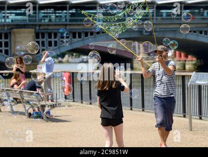 London, England, UK. Street entertainer on the South Bank blowing bubbles for children to chase Stock Photo