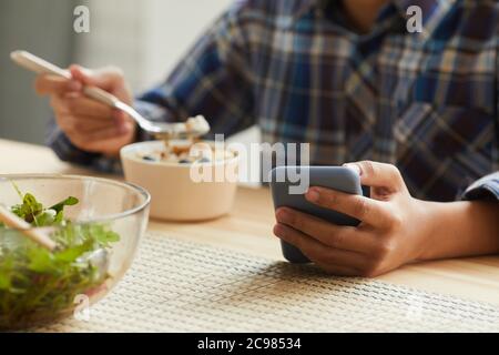 Close-up of boy eating at the table and using his mobile phone in the kitchen Stock Photo