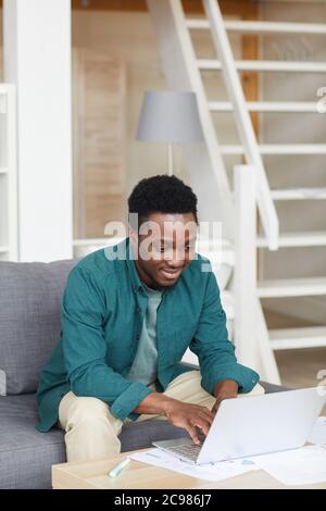 African young man sitting on sofa and typing on laptop computer he working online at home Stock Photo