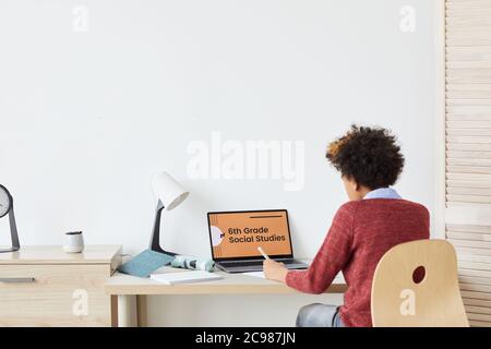 Rear view of African boy sitting at desk in front of laptop and looking at monitor he studying online at home Stock Photo