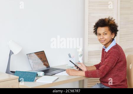 Portrait of African schoolboy smiling at camera while sitting at desk in front of laptop and studying at home Stock Photo