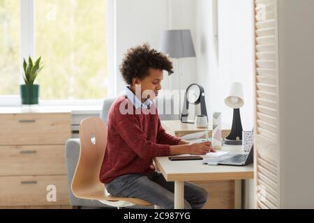 African schoolboy sitting at his desk doing his homework and preparing for the lessons in the room at home Stock Photo