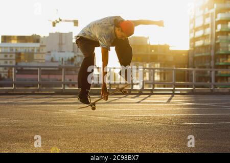 Skateboarder doing a trick at the city's street in summer's sunshine. Young man in sneakers and cap riding and skateboarding on the asphalt. Concept of leisure activity, sport, extreme, hobby and motion. Stock Photo