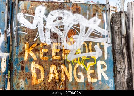 Danger keep out rough painted sign on decaying rusty metal gates in Southend on Sea, Essex, UK. Warning message outside dangerous site Stock Photo