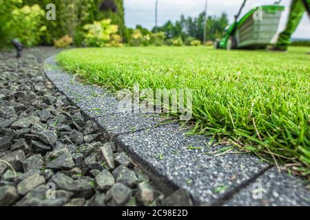 Backyard Lawn Grass Field Cobble Edge. Grass Mowing and Edges Finishing. Gardening and Landscaping Industry Theme. Stock Photo