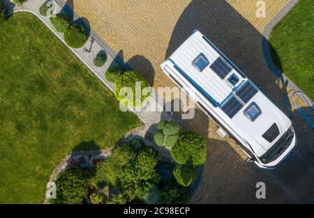 Camping and Tourism Theme. Modern Camper Van with Solar Panels Installed Staying on Cobble Stone Driveway Awaiting New Destination. Aerial View Stock Photo