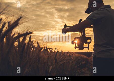 Cinema and Stock Footage Production. Caucasian Video Camera Operator in His 40s with Gimbal Stabilization Taking Steady Scenic Sunset Shot Between Rye