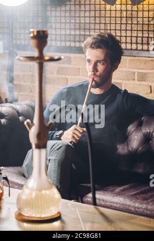 young man is watching a performance and smoking hookah. close up shot.smoking ban. heavy smoking Stock Photo