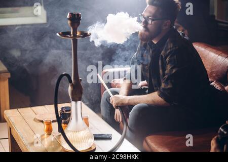 brutal handsome ginger man is smoking hookah in the bar. close up side view shot. free time, hobby, interest Stock Photo