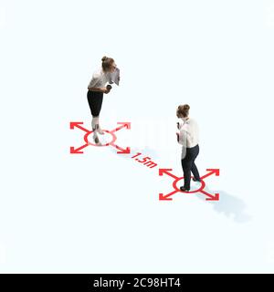 Studio shot of people demonstrating social distancing with arrows indicating the separation. Office workers during coronavirus outbreak with new rules for safety and healthcare. High angle view, copyspace. Stock Photo