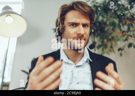 Close up portrait of an angry businessman with headset having stressful online conversation Stock Photo