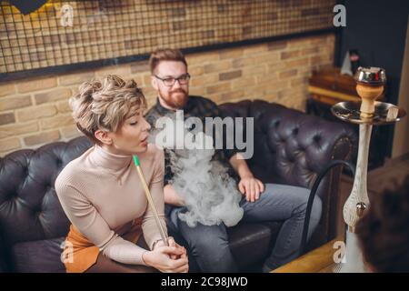 cheeerful ginger man is looking at blond girl who is smoking hookah. closeup photo. love. guy is falling in love Stock Photo
