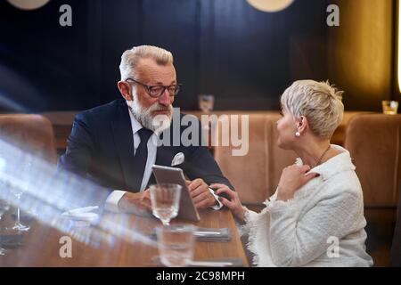 Beautiful senior couple looking at the same tablet in restaurant, public concept, caucasians mature use modern technology Stock Photo