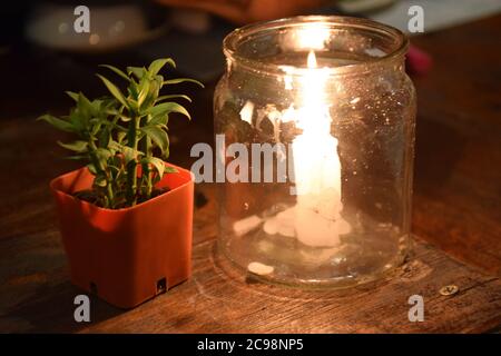 Candles in glass jar in glass and small tree in pot on Dinner Table Stock Photo