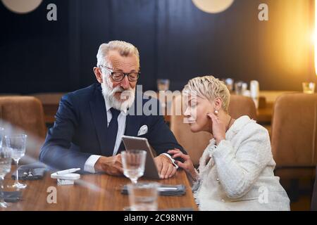 Beautiful senior couple looking at the same tablet in restaurant, public concept, caucasians mature use modern technology Stock Photo