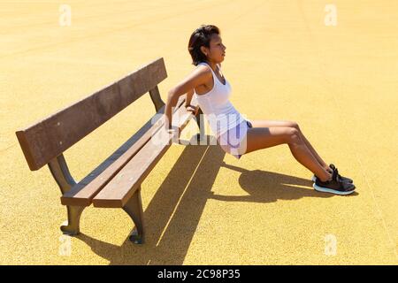 Young woman exercising her body with the help of a bench. She's in an outdoor park. Space for text. Stock Photo