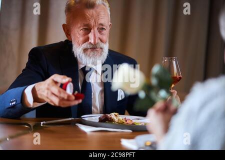 Caucasian gray-haired man in tuxedo offers to get married. Lovely face of male. Woman keep white rose in hands Stock Photo