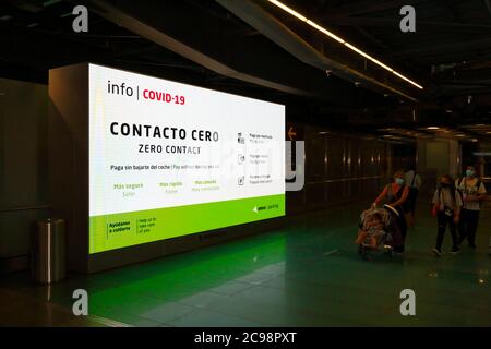 28th July 2020, Barajas Airport, Madrid, Spain: Passengers walk past a Covid-19 information sign in the departure lounge area of the Terminal 4S building of Barajas Airport. Reduced numbers of flights are now operating between European countries after the lockdown to control the covid-19 coronavirus, and governments have put a system of air bridges in place to facilitate travel and tourism. Spain has seen a number of new outbreaks in recent days, prompting the UK government to announce that people returning to the UK from Spain should quarantine for 14 days on arrival. Stock Photo