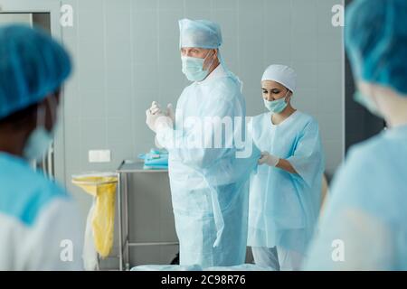 attractive assistant helping the talented old surgeon to put on sterile clothing.close up side view photo. Stock Photo