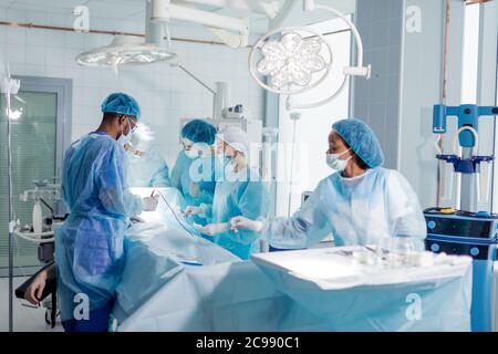 mixed race technicians, anesthetists carry out surgery in the clinic. Stock Photo