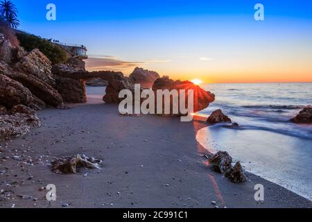 Sunrise on the Spanish coast. Balcon Europa in the city of Nerja on the Costa del Sol. Sea and rocks with arch on coastline in Andalusia. Sandy beach Stock Photo