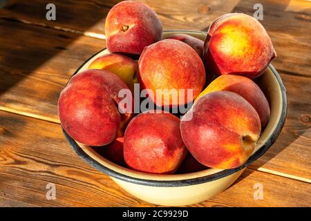 ripe peaches in an iron bowl on a wooden background in bright sunlight Stock Photo
