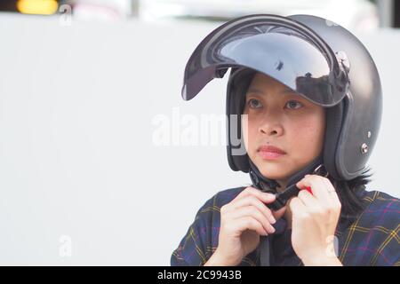 A Young Woman fastening or Wearing her motorbike helmet with blur Fukien tea tree Carmona retusa green background - Zero accident concept Stock Photo