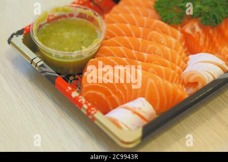 Soft Focus to Sashimi salmon topping with Parsley and Thai Seafood Dipping Sauce on Japanese Plastic Plates Stock Photo