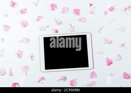 Flat lay composition electronic tablet with empty display among pink petals of peony flowers on white background. Stock Photo