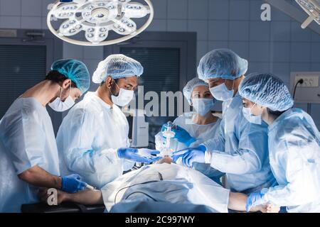 Pre oxygenation for general anesthesia. Focused surgeon team operating in an operating theatre, blue filter Stock Photo