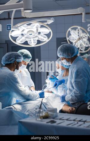 Urgent surgery. Professional smart intelligent surgeons standing near the patient and performing an operation while saving his life. Professional trea Stock Photo