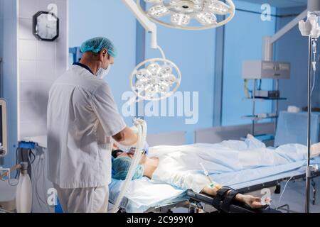 Assistant holds mask and induction for general anesthesia over patient head, getting ready to Surgery. Stock Photo