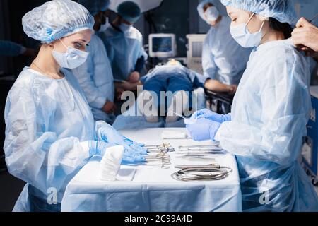 Nurse s hands holding surgical instruments and tools, close up including scalpels, forceps and tweezers arranged on a table. Surgeons at work in opera Stock Photo